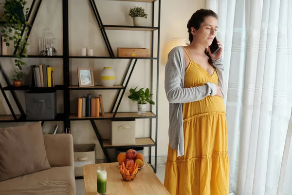 Vážná Těhotná Mladá Žena Stojí Okna Mluví Telefonu — Stock fotografie