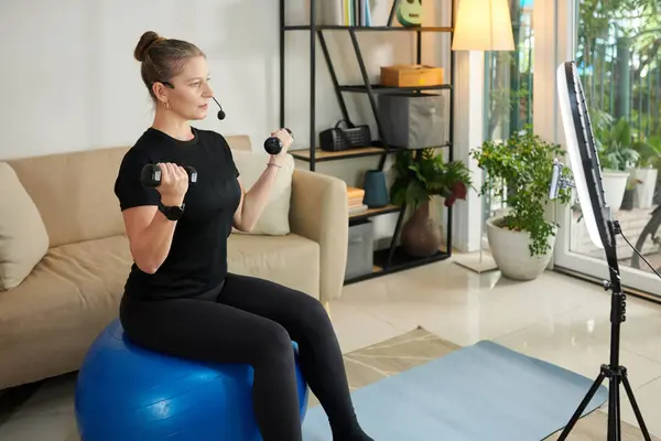 Female online personal trainer showing how to exercise with dumbbells to get stronger arms