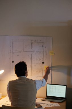 Masasının üstündeki duvarda asılı olan sarı etiketlere fikirler yazan bir mimar.