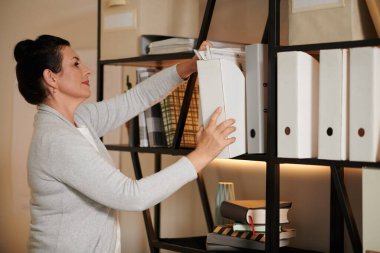 Büro 'daki raflarda belge arayan olgun bir mimar.