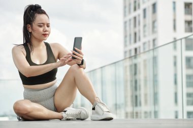 Sporcu kadın eğitimden sonra dinleniyor ve telefonundaki mesajlara cevap veriyor.