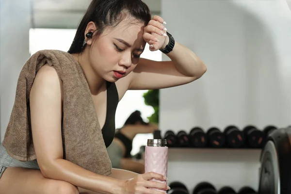 Sweaty sportswoman drinking water after training in gym