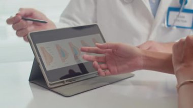 Dijital tablet kullanarak göğüs büyütme ameliyatını tartışan tanınmayan kadın hasta ve doktorun ellerini kapatın.