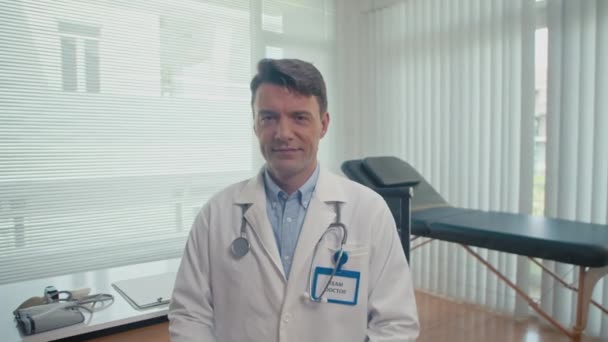 診療所で患者を待っている間 バッジとステスコープを身に着けている白いラボコートの陽気な医療従事者の肖像 — ストック動画