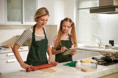 Zencefilli kurabiye için hamur toplarken anne ve kızı yemek tarifine uyuyorlar.