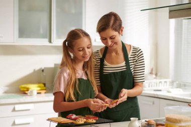 Gülümseyen anne ve kız kutlama için pişirdikleri çikolatalı kurabiyelere bakıyorlar.