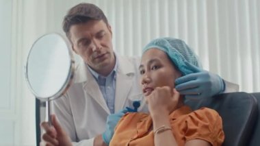 Kadın Asyalı hastanın klinikte estetik cerrahla yüz gerdirme ameliyatının sonuçlarını tartışırken orta boy fotoğrafı.