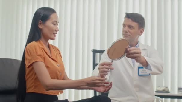 診療所の化粧品手順の後に女性患者に鏡を与える男性医師の中長いショット — ストック動画