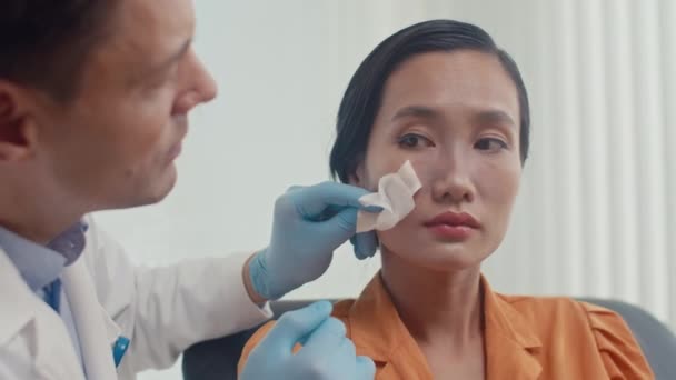診療所の手術後の女性患者の鼻を見る白いコートの男性医師のメディア閉鎖 — ストック動画