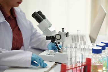 Modern laboratuarda profesyonel mikroskopla çalışan ilaç bilimcisinin kırpılmış görüntüsü.