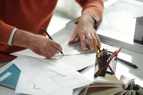 Hands of construction engineer drawing house blueprint at his office desk