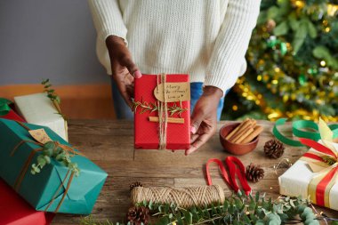 Genç bir kadının, arkadaşı için paketlediği Noel hediyesini kestiği görüntüsü.