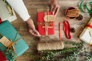 Aile fertleri için paketlenmiş ve dekore edilmiş küçük Noel hediyelerini gösteren kadınların elleri