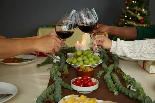 Friends toasting with wine glasses over Christmas dinner table when celebrating at home