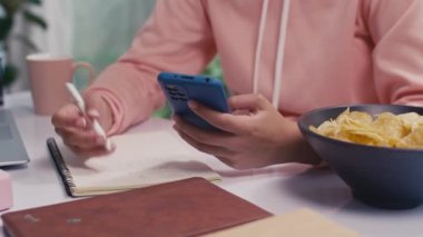 Akıllı telefon kullanarak sınava hazırlanan ve evde ders çalışırken not alan genç kızların orta boy fotoğrafları.