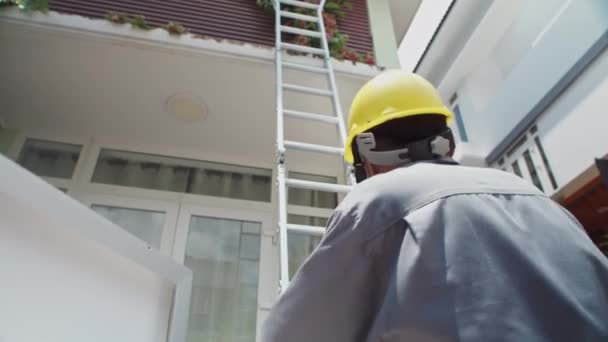 彼の共同作業者が梯子を使用して屋根に太陽電池パネルを持ち上げるのを助ける専門家の低い角度の眺め — ストック動画