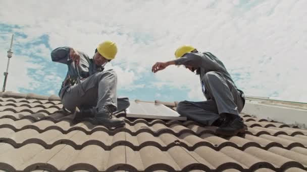 两个戴着硬礼帽的建筑商在房顶上工作 同时在客户住房上安装太阳能电池板的低视角图像 — 图库视频影像