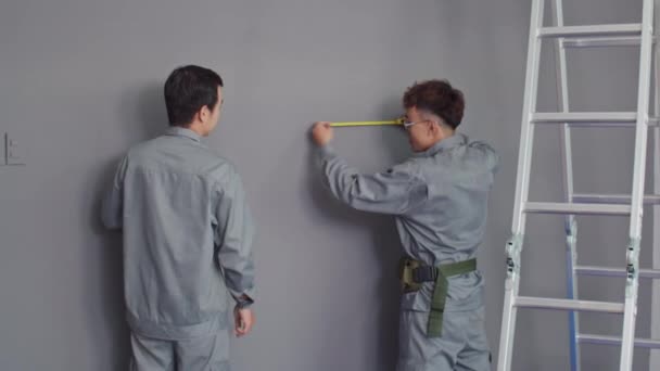 Średniej Długości Ujęcie Pary Robotników Budowlanych Szarej Jednolitej Ścianie Pomiarowej — Wideo stockowe