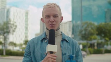 Sokakta haber çekerken mikrofonlu bir erkek muhabirin orta boy görüntüsü.