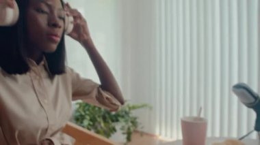 Orta boy Afrika kökenli Amerikalı kadın podcaster. Kulaklık takıyor ve stüdyoda kayıt yaparken sesi ayarlıyor.