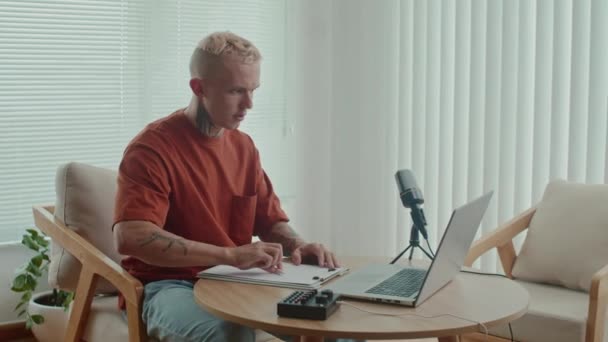 集中的男性博客作者坐在笔记本电脑和话筒前创作他的播客剧本的中长镜头 — 图库视频影像