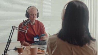 İş kadınının omzundan, erkek basın sözcüsünün sorularını cevaplıyor kulaklık takıyor ve stüdyoda akıllı telefona bakıyor.