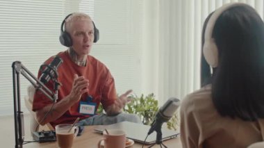 Erkek pozitif gazetecinin, stüdyo röportajı sırasında masada oturan ve mikrofona konuşan kadın konuğun elini sıkarkenki orta pozu.