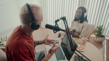 Yüksek açılı kulaklıklı erkek podcaster stüdyodaki görüşme sırasında bayan konukla konuşuyor.