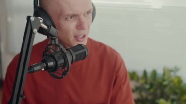 Erkek gazetecinin kulaklıkla stüdyoda kayıt yaparken mikrofona konuştuğu orta boy bir fotoğraf.