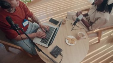 Talk Show konuğunun yukarıdan aşağı görünümü soruları cevaplarken sunucu yuvarlak masada otururken dizüstü bilgisayardan notlar alıyor