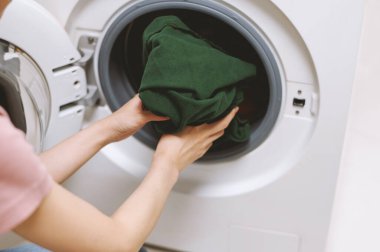 Çamaşır makinesinden temiz giysiler çıkaran genç bir kadın.