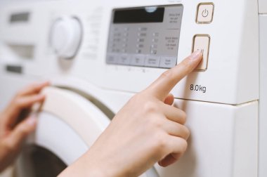 Çamaşır makinesinde çamaşır makinesini çalıştırmak için düğmeye basan kadının yakın plan resmi