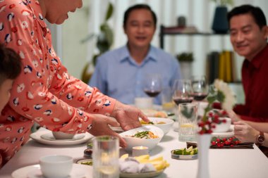 Vietnamlı son sınıf öğrencisi kadın yemek masasına geleneksel aperatiflerle kase koyuyor.