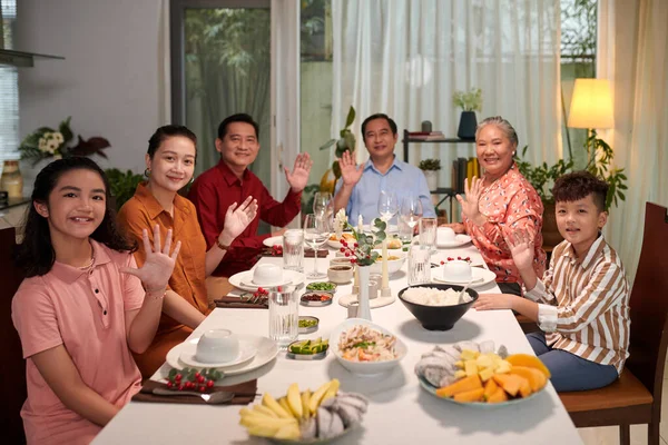 Big Vietnamese family sitting at dinner table and waving at camera