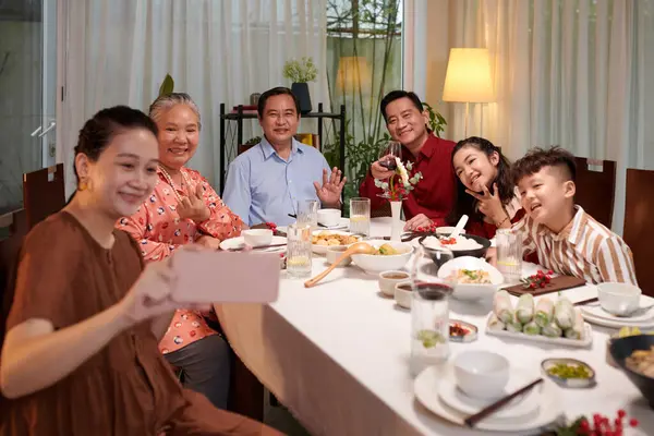 Cheerful big Vietnamese family posing for selfie at dinner table