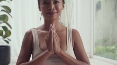 Evde meditasyon yaparken el ele tutuşup kameraya bakarken gülümseyen Asyalı kadının portresi.