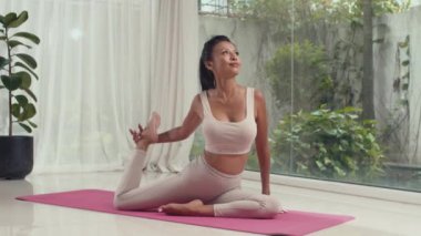 Asana 'da, evde yoga yaparken bacaklarını, kollarını ve vücudunu esneten genç ve esnek bir kadının uzun pozu.
