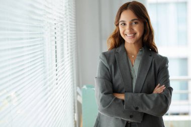 Ofis penceresinde duran gri ceketli başarılı kadın girişimcinin portresi.
