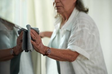 Televizyondaki tozları silen yaşlı bir kadın görüntüsü.