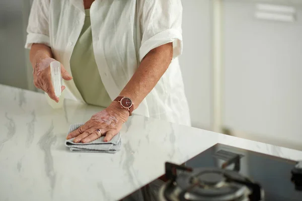 Hands of aged woman wiping counter with cleaning detergent
