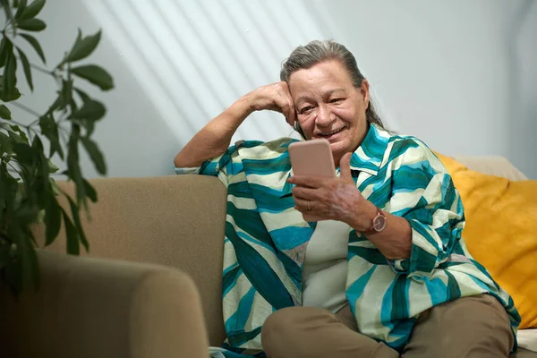 Cheerful elderly woman video calling grandchild to discuss news