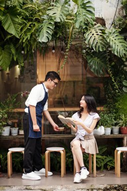 Gülümseyen garson dışarıdaki masada oturan genç bayana kahve getiriyor.