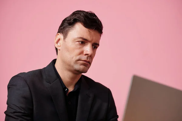 ピンクで隔離されたラップトップスクリーン上の深刻なビジネスマンの読書記事の肖像画 — ストック写真