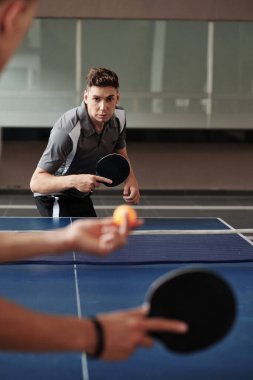 Spor salonunda arkadaşlarıyla masa tenisi oynayan ciddi bir genç adam.