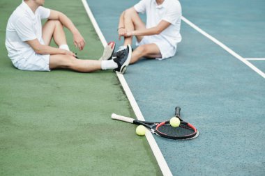 Tenis raketleri ve topları, maçtan sonra dinlenen sporcuların yanında.