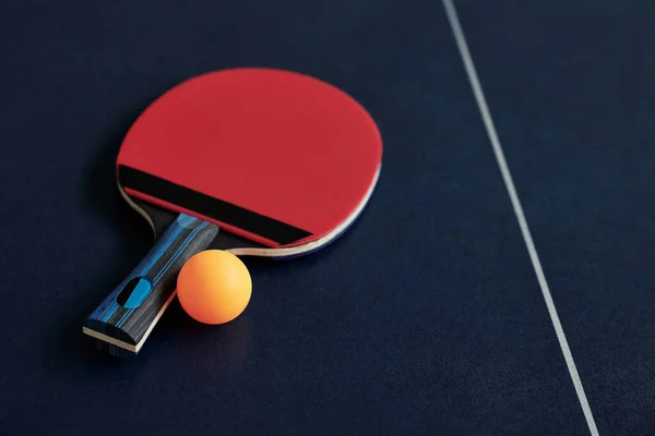 Red table tennis racket and orange ball on table, selective focus