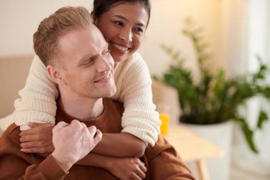 Gülümseyen Asyalı kadın, mutlu erkek arkadaşına arkadan sarılıyor.