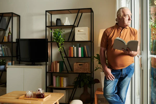 Pensiv Senior Man Med Öppen Bok Händerna Tittar Genom Fönstret — Stockfoto