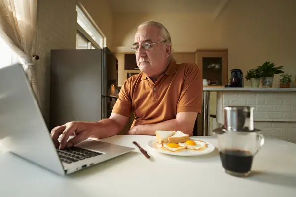 Starší Muž Brýlích Doma Snídani Kontroluje Maily Notebooku — Stock fotografie