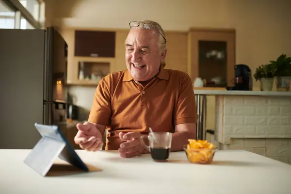 Happy elderly man drinking coffee and video calling friend or family member